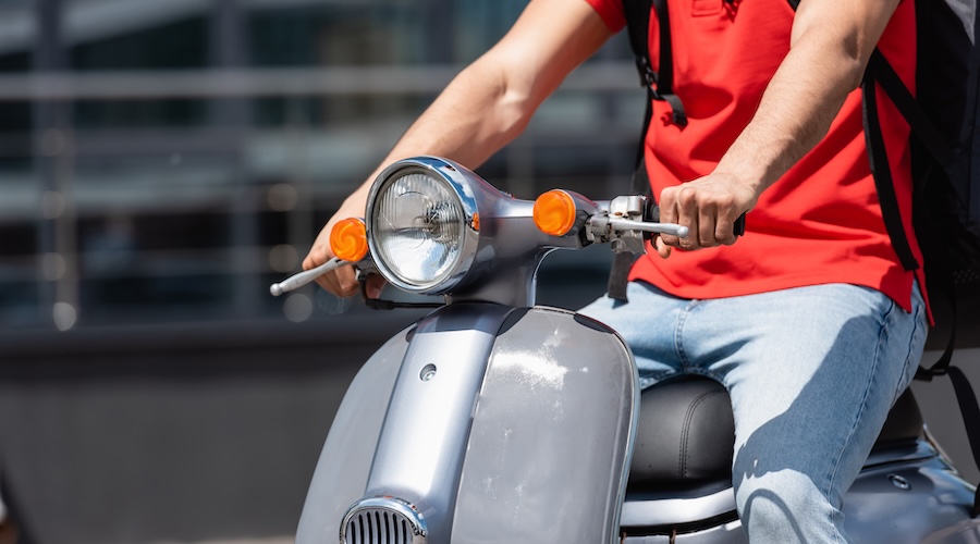 Cropped view of courier with backpack driving scooter outdoors